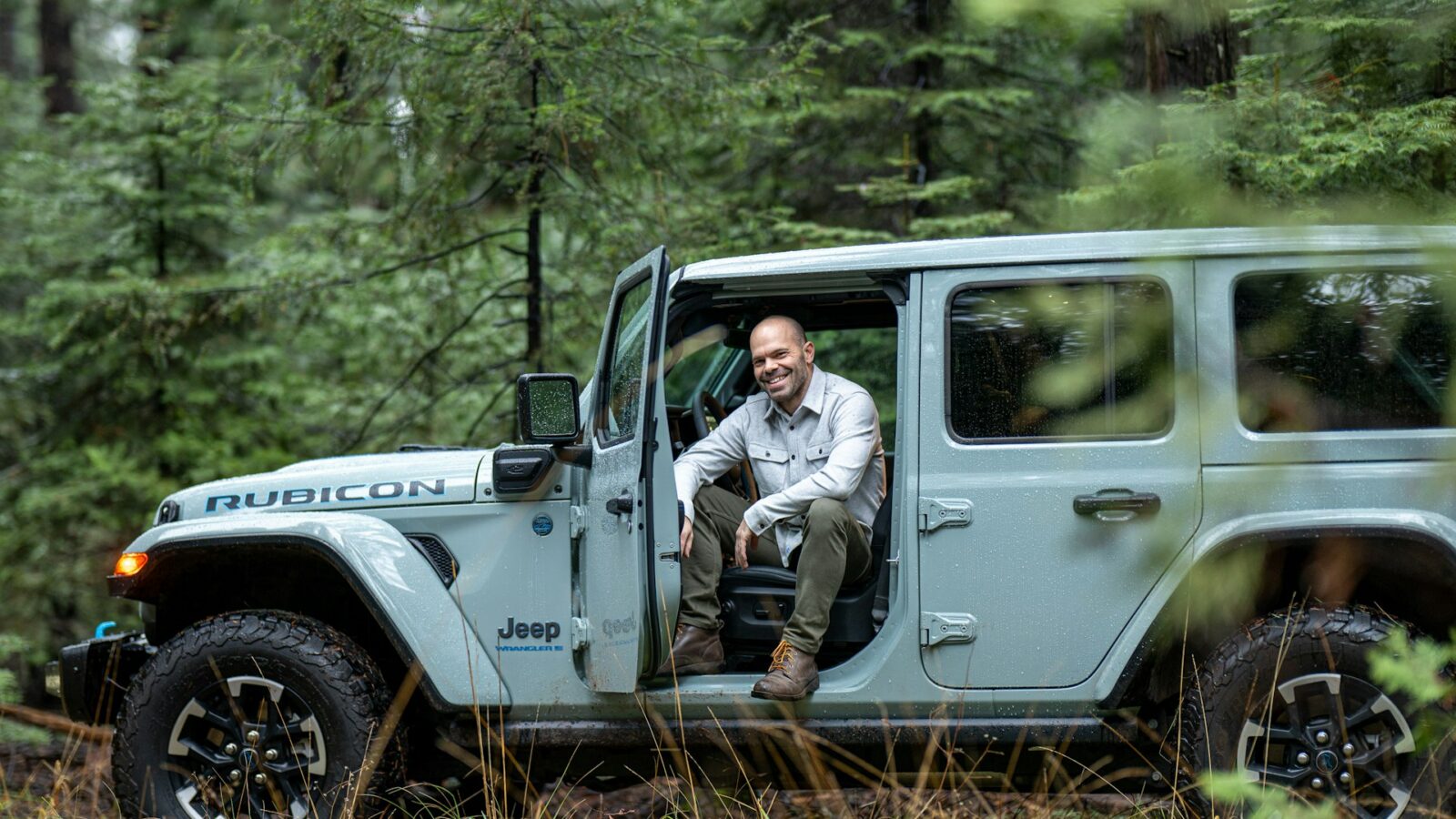 Man sitting in the open driver door of a Jeep Wrangler Rubicon in a forest