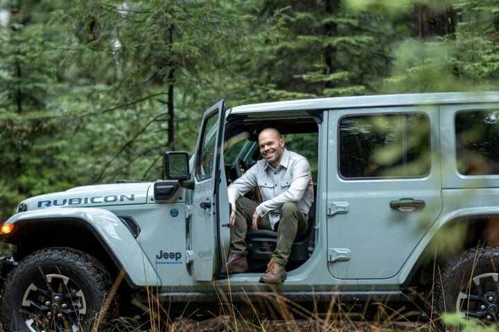 Man sitting in the open driver door of a Jeep Wrangler Rubicon in a forest