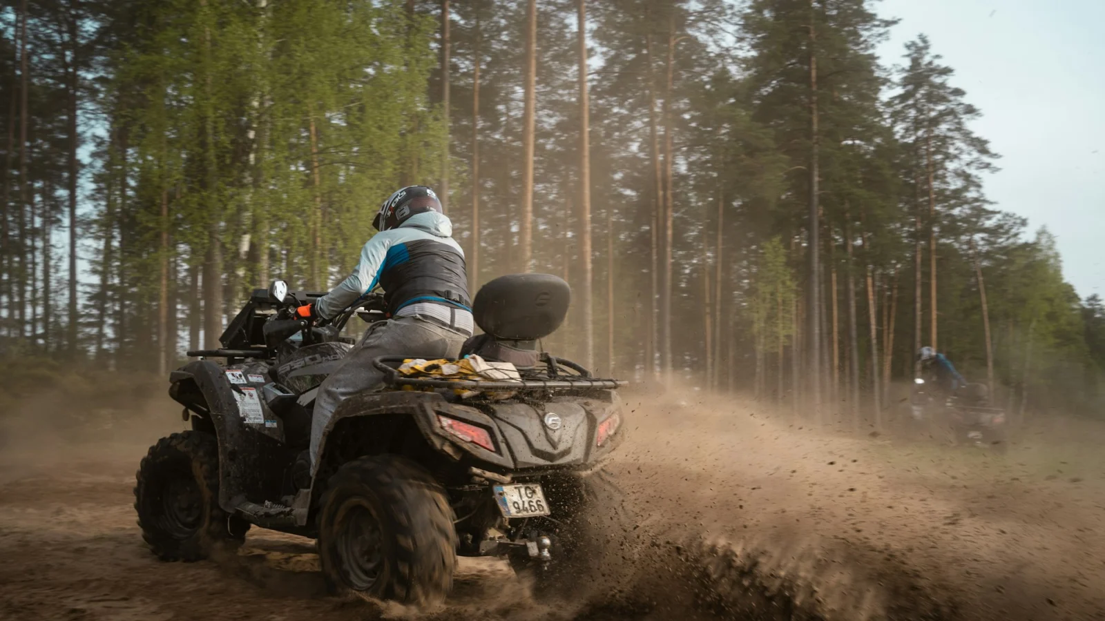 Rider on a utility ATV raising dust on a forest track