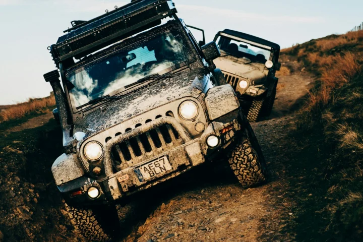 Two mud-covered Jeep Wranglers climbing a dirt trail
