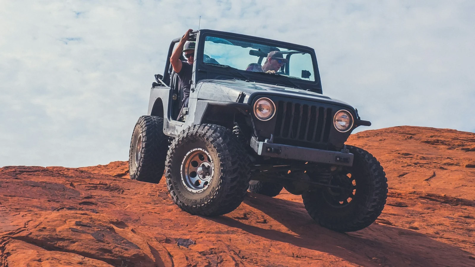 Jeep Wrangler with its doors off climbing red slickrock