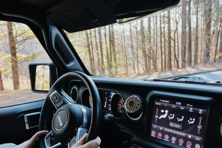 Driver with both hands on the wheel of a Jeep Wrangler JL on a forest road