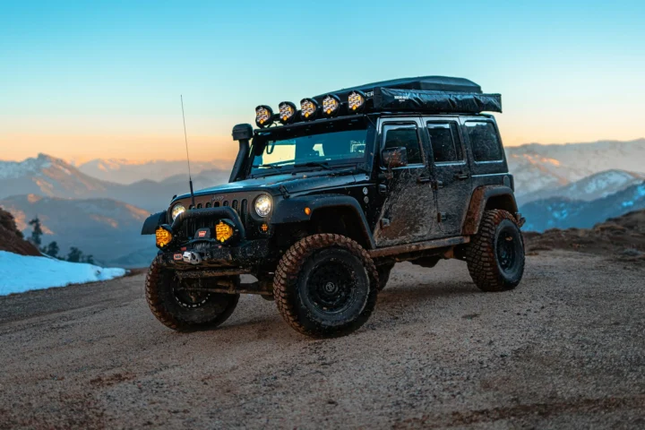 Jeep Wrangler with roof lights on a mountain dirt road at dusk