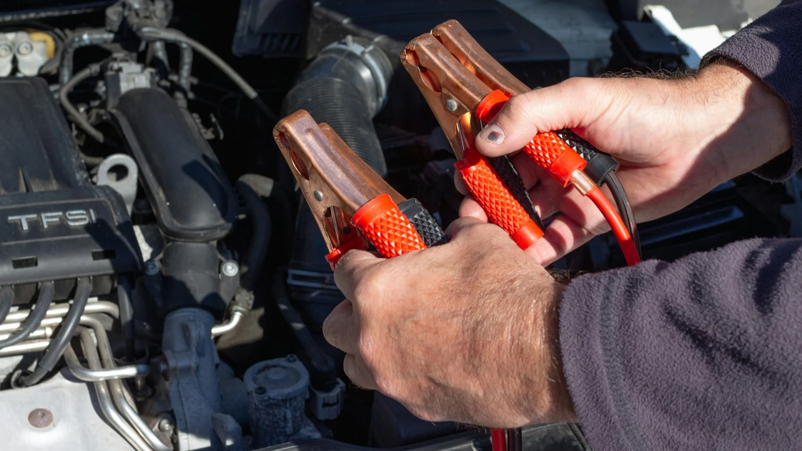Hands holding jumper cable clamps over an engine bay