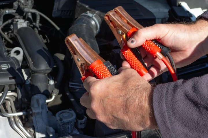 Hands holding jumper cable clamps over an engine bay